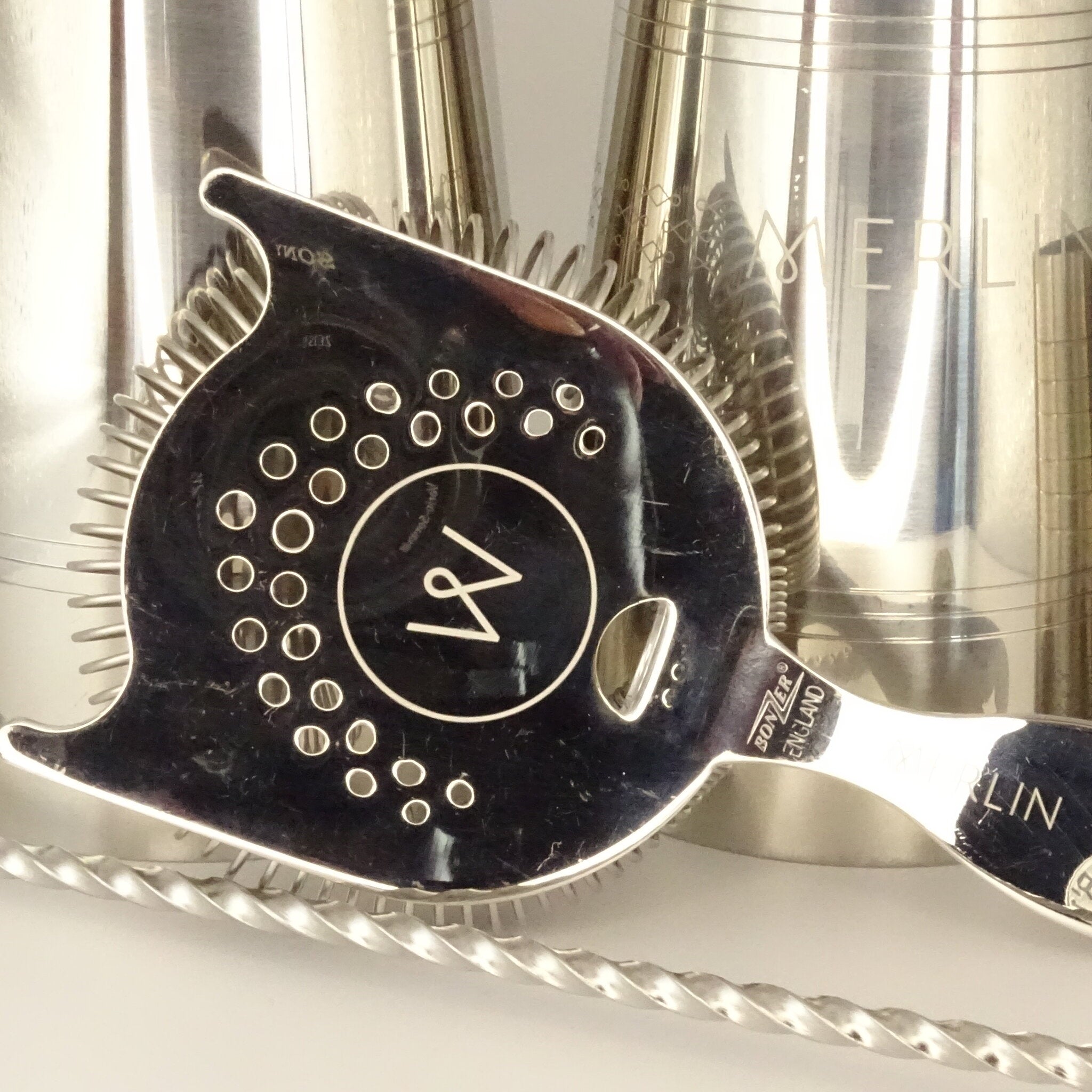 Close up of cocktail tools including shakers, a hawthorne strainer and bar spoon.