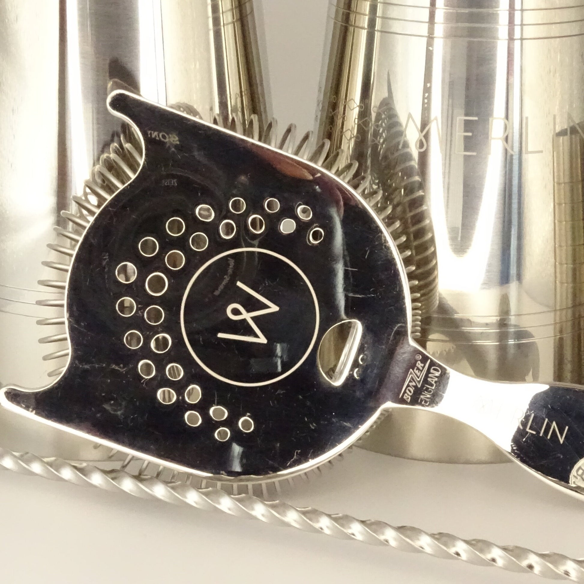 Close up of cocktail tools including shakers, a hawthorne strainer and bar spoon.